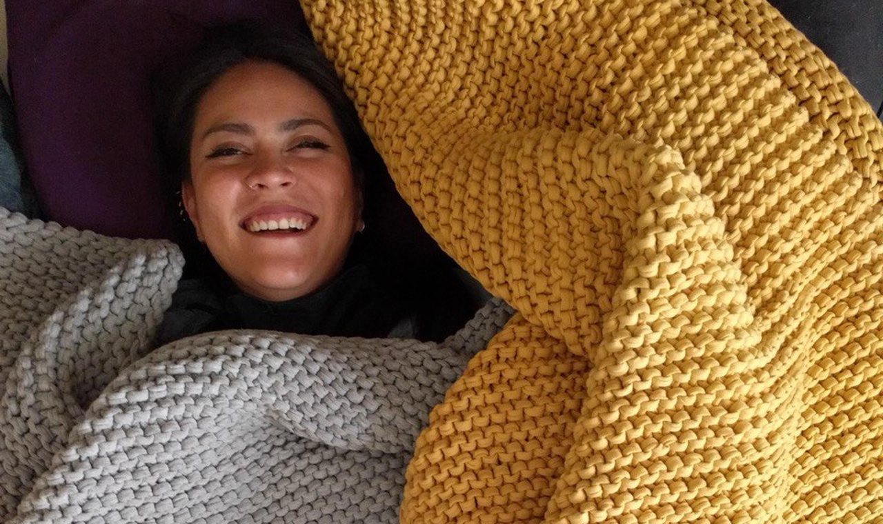 Mujer tumbada en un sofá, cubierta con mantas gruesas de punto